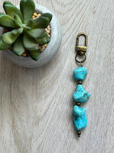 Load image into Gallery viewer, A handmade turquoise nugget zipper pull with antique bronze findings, displayed next to a potted plant.